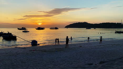 Wide,-Time-Lapse-shot-of-a-beach-line,-and-silhouette-of-people-playing-with-an-ocean-and-orange-color-sunset-in-the-background