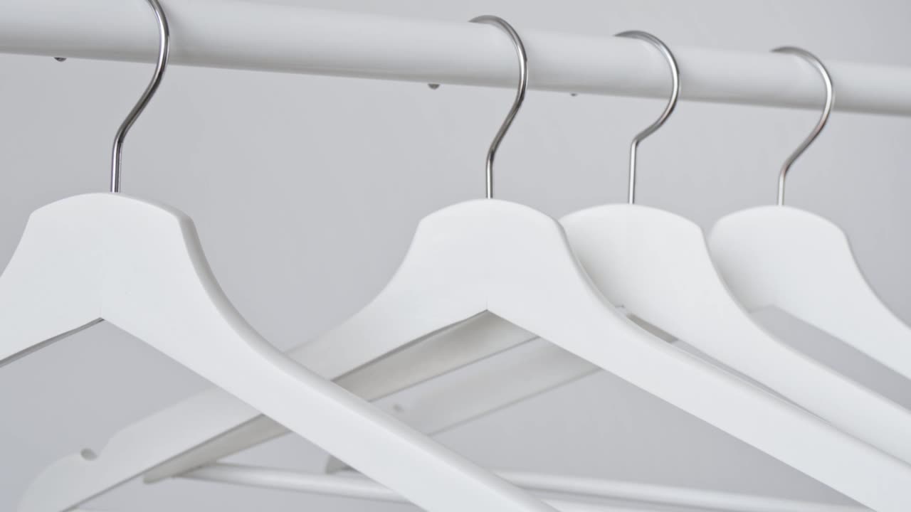 la mano de la mujer cuelga blanca vacía percha de ropa de madera en el estante sobre fondo de pared blanca. venta en la tienda, descuentos, publicidad minimalista. moda, elegantes perchas de gancho de metal. equipos para el hogar