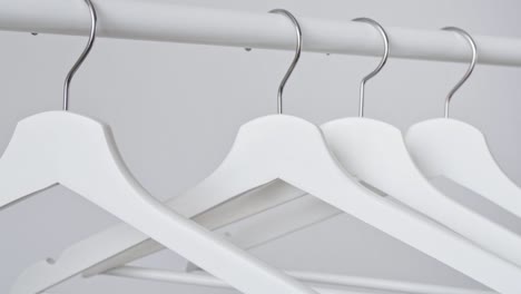 woman's hand hangs white empty wooden clothes hanger on rack on white wall background. sale in the store, discounts, minimalistic advertising. fashion, stylish metal hook hangers. equipment for home