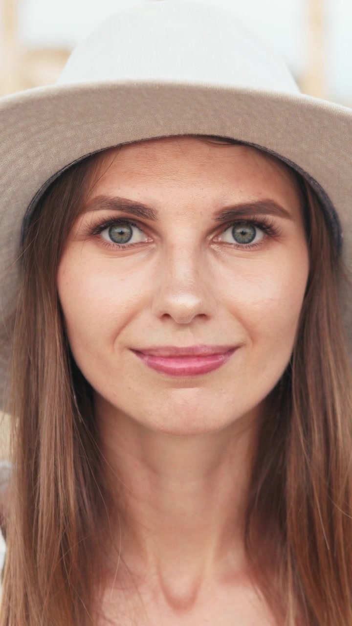 Una bella donna con gli occhi azzurri che indossa un cappello sorride alla telecamera, video verticale