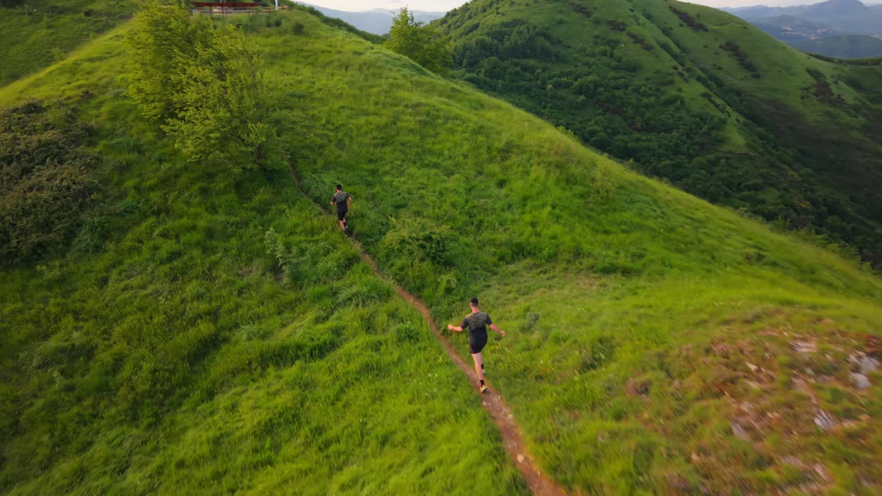 Two men running on a green hill trail in the mountains, active and free