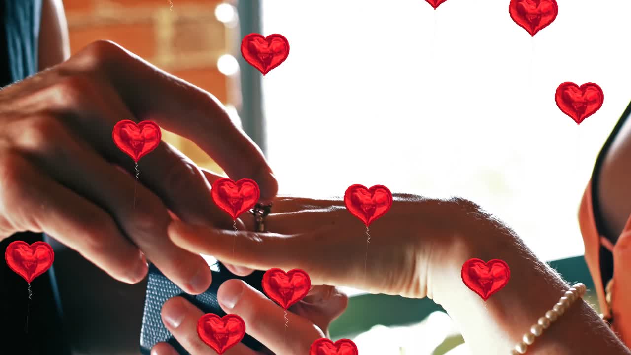Multiple heart balloons floating against mid section of man putting ring on woman
