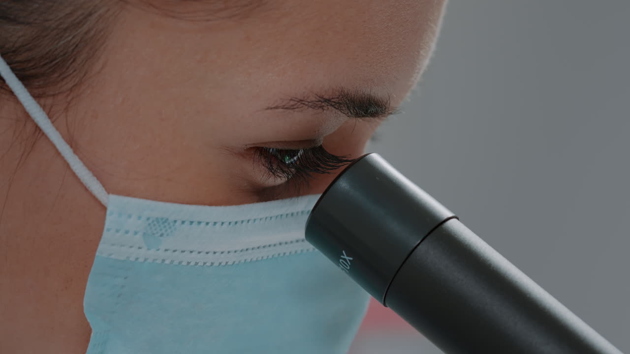 Biologist with face mask using microscopic lens on chemistry tool