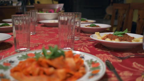 Cámara-Lenta-De-Una-Mesa-Bien-Preparada,-La-Pasta-Se-Sirve-En-Los-Platos-Con-Un-Mantel-Rojo