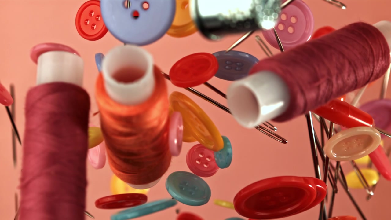 Colorful Sewing Buttons, Thread, and Needles Floating on Pink Background
