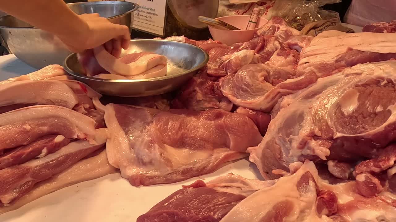 Close-up of hands organizing various cuts of raw meat on a market table with metal bowls.