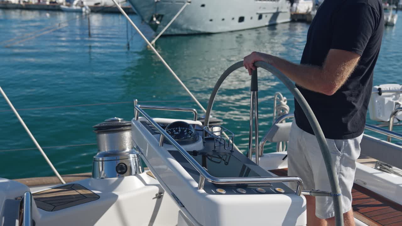 Unrecognizable man holding steering wheel helm of sailboat in port