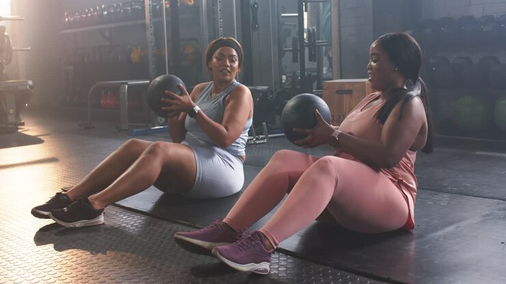 Verschiedene Freundinnen drehen und geben einen schwarzen Medizinball im Fitnessstudio weiter, um die Körpermitte zu stärken