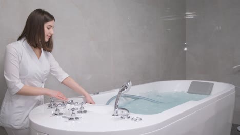 a female spa specialist fills a bathtub with hot water for a hydromassage procedure. professional hydromassage.