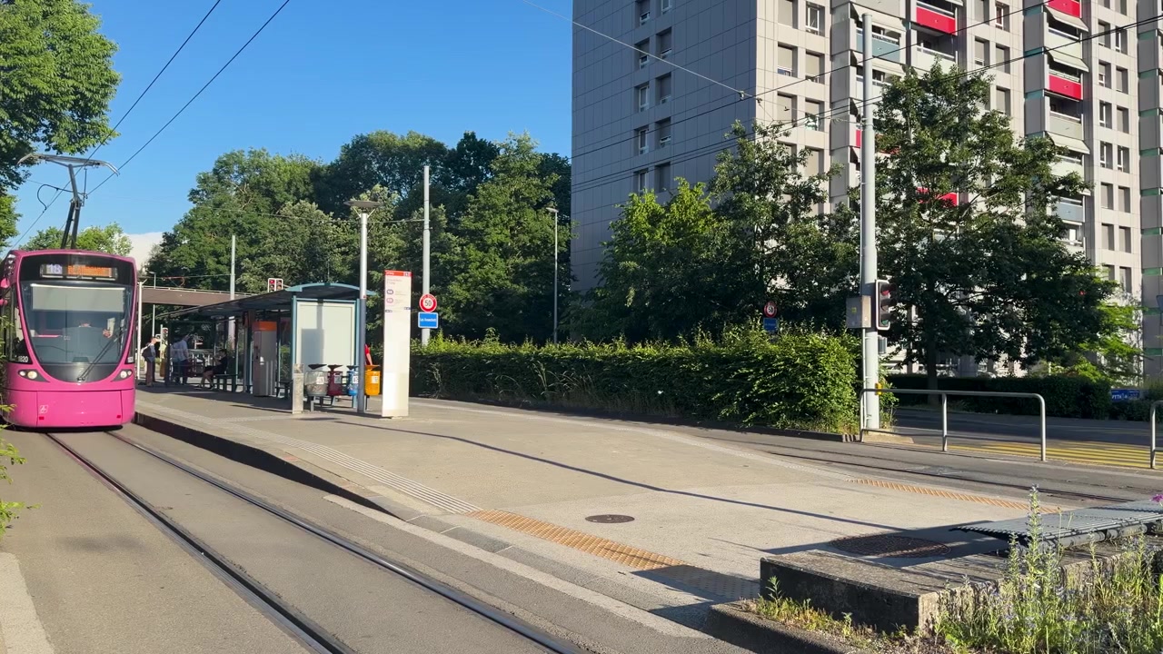 Un tram rosa si avvicina a una moderna piattaforma di transito sotto la luce solare intensa in un ambiente urbano.