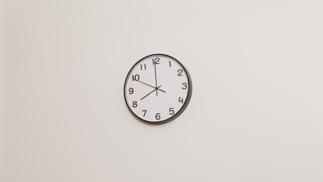 Un'inquadratura a campo largo di un semplice orologio da parete con cornice nera e quadrante bianco, che indica le 8:00.