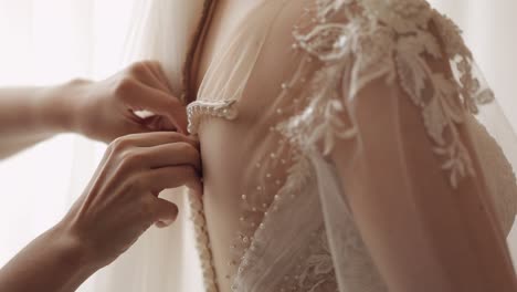 Bridesmaid-ties-and-helps-put-on-wedding-dress,-morning-preparation-of-the-bride-with-white-gown