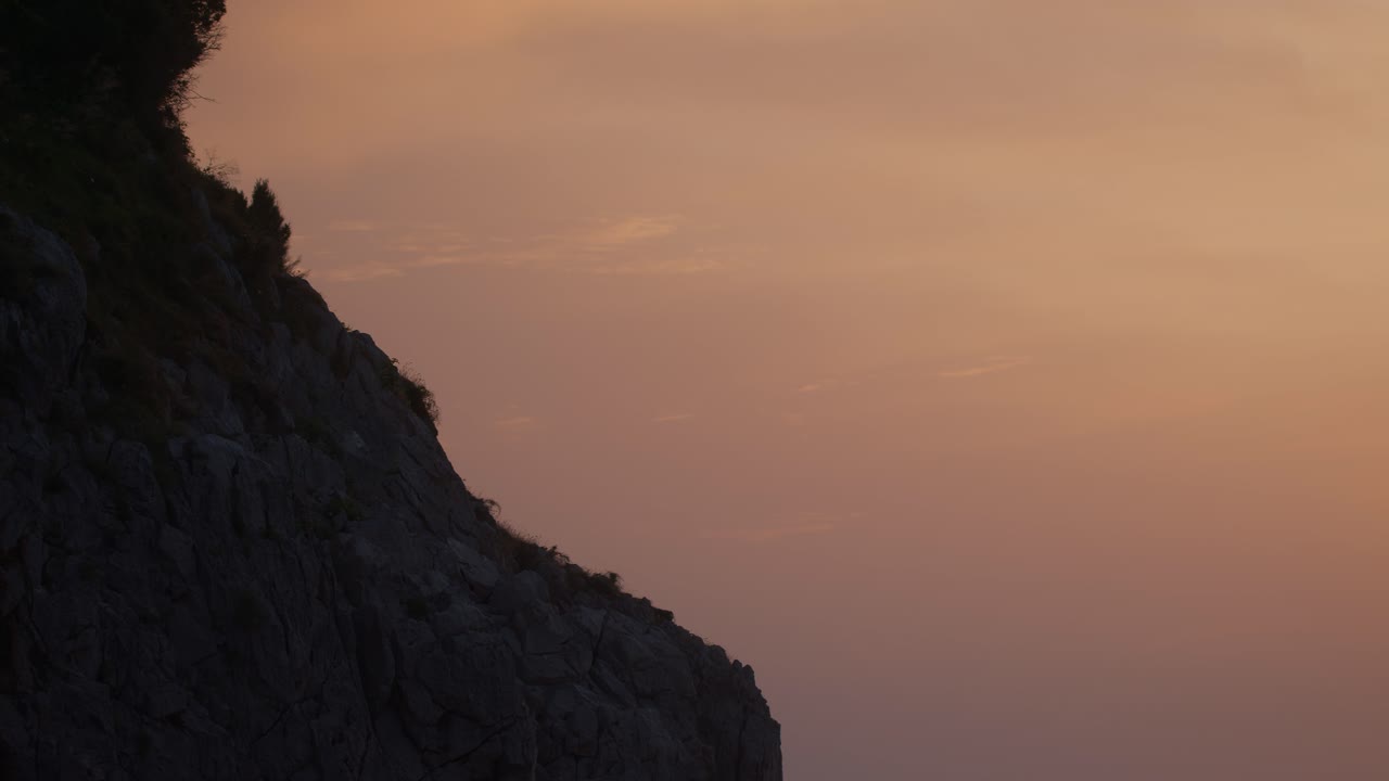 Silhouette of a rocky mountain with birds flying around it during a vibrant orange sunset in Anacapri