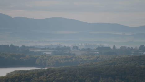 aerial view of a timelapse of a forest and a river swept by the shadows of clouds with a foggy mountain in the background