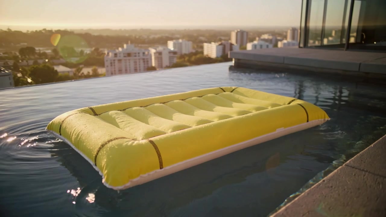 Pulling back cam showing yellow air mattress floating on rooftop infinity pool, to reveal skyline