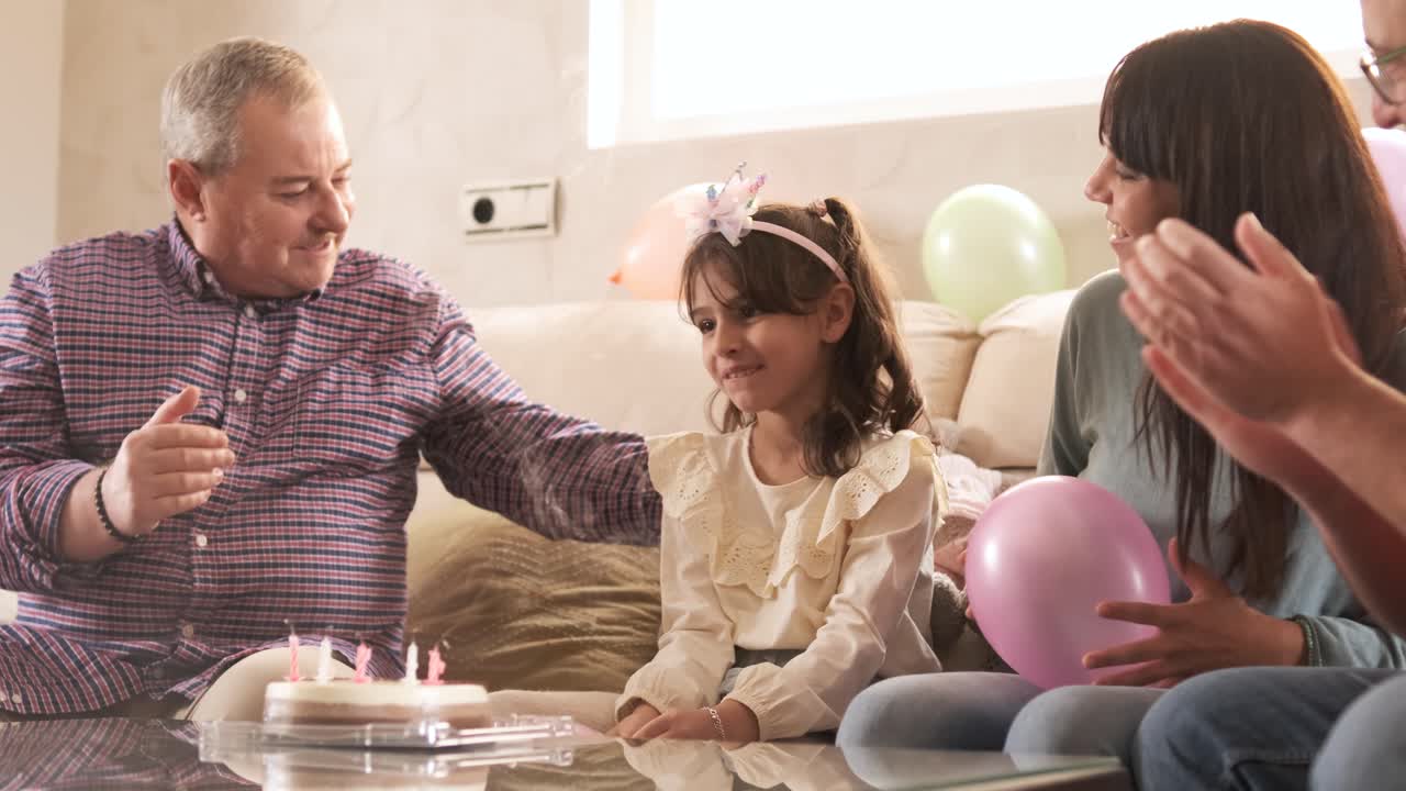 Family singing while a girl blowing the candles of her birthday cake