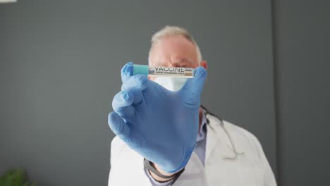 Portrait-of-caucasian-senior-male-doctor-wearing-face-mask-holding-covid-19-vaccine