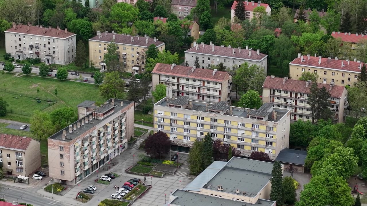 Letecký pohled na hustý obytný bytový komplex v předměstské čtvrti, obklopený bujnými zelenými stromy a infrastrukturou.