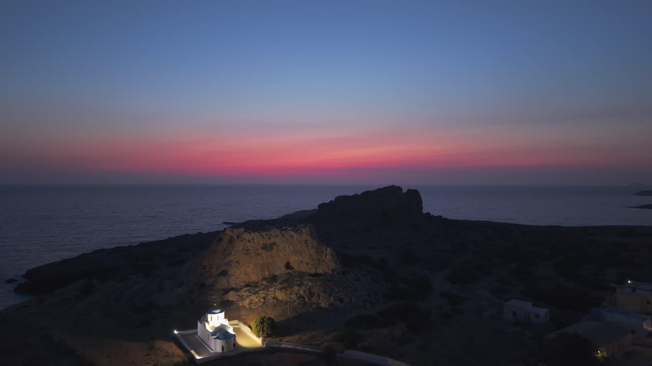 Cinematic drone shot at twilight revealing the picturesque lit fishing village of Finiki in Karpathos, with its harbor, boats, and Mediterranean charm