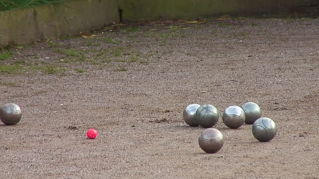 P&eacute;tanque boules rolling up towards a red coach during a p&eacute;tanque league game