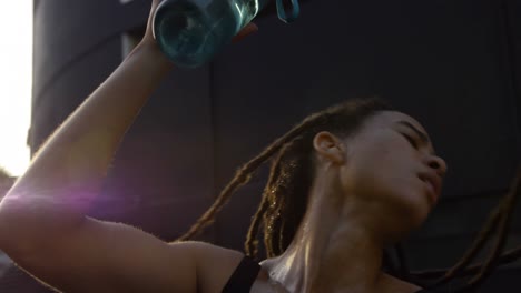 Front-view-of-young-African-American-woman-pouring-water-on-her-head-in-the-city-4k