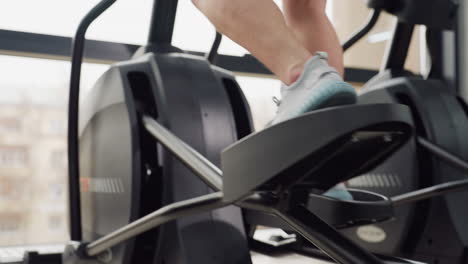 close up leg view of fitness fanatic powering up elliptical trainer pedal with explosive drive during intense indoor cardio session in well lit modern gym with sleek equipment and urban view