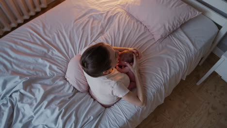 mother cuddling newborn baby in bed