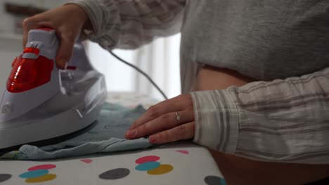 pregnant woman irons baby bodysuit while gently holding her belly at home