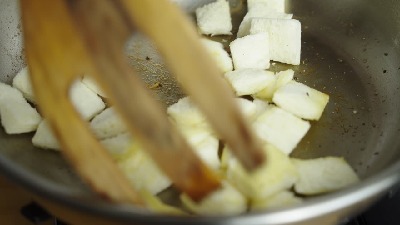 Frying bread pieces for Caesar salad inside frying pan