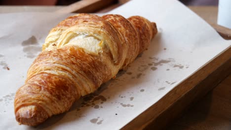 a hand reaching for a freshly baked croissant on a wooden tray