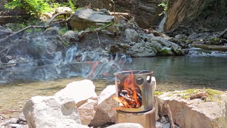 hobo cooker is burning in nature with waterfall and river in background