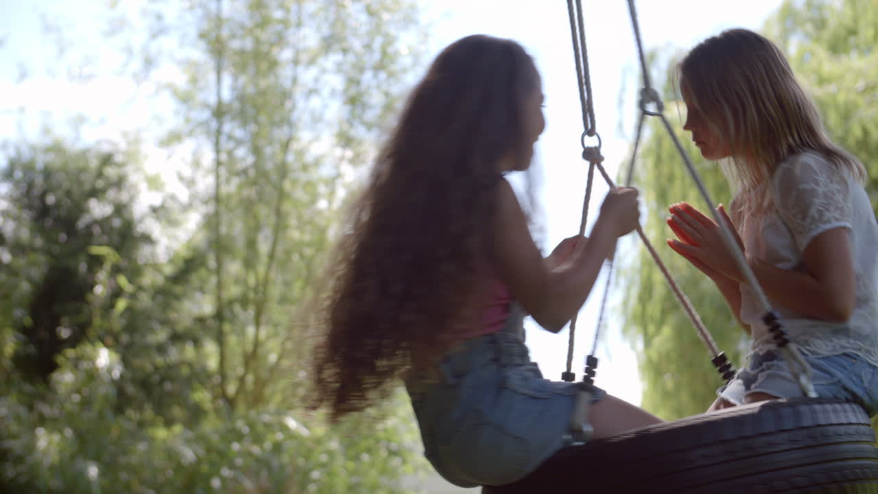 dos niñas jugando en el columpio de neumáticos en el jardín