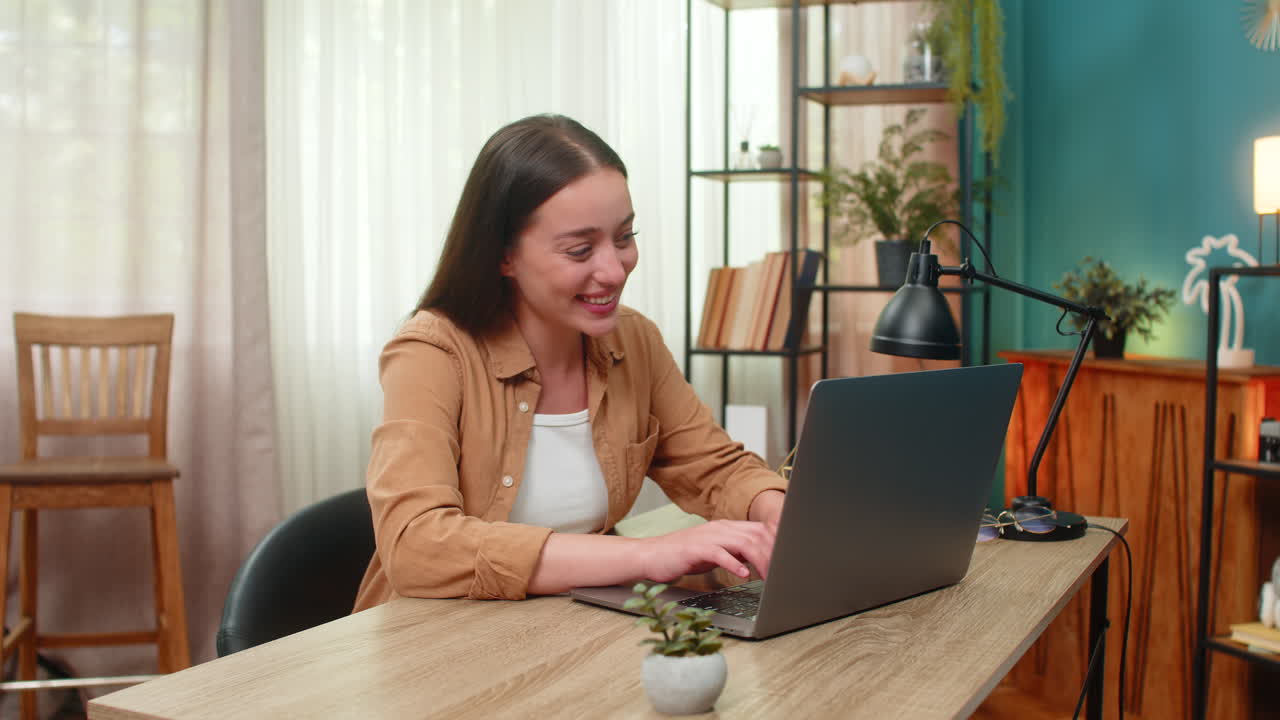 Young woman opens laptop smiles proudly after seeing project results celebrating achievement at desk