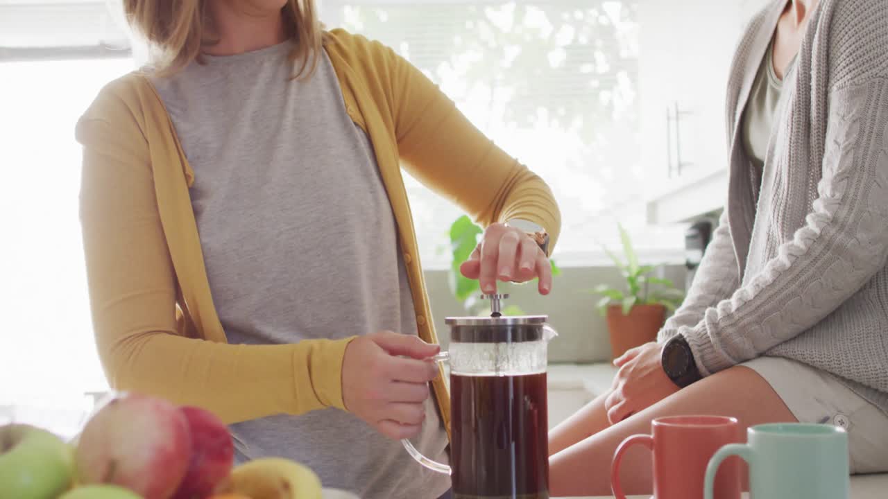 백인 레즈비언 커플이 집 주방에서 함께 커피를 마시고 있습니다.