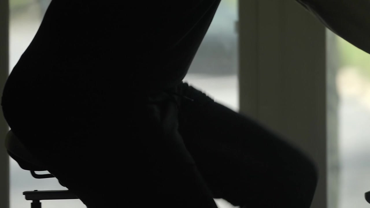 Athlete exercising on stationary bicycle, silhouette in home