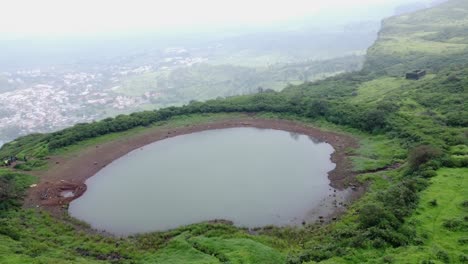 Cinematic-aerial-view-of-the-sacred-lake-at-Brahmagiri-hill-in-the-Western-Ghats-of-Maharashtra-during-monsoon-with-the-view-of-Trimbak-town-in-the-background,-Nashik,-India