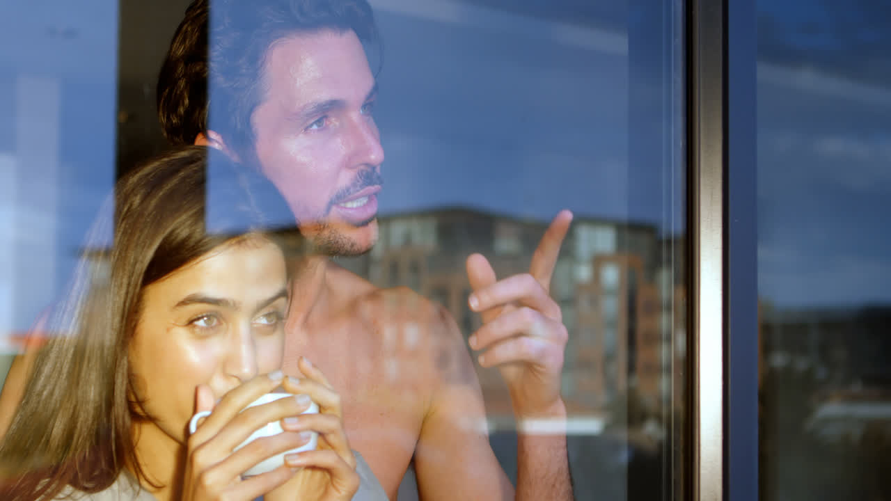 pareja mirando por la ventana mientras beben café 4k