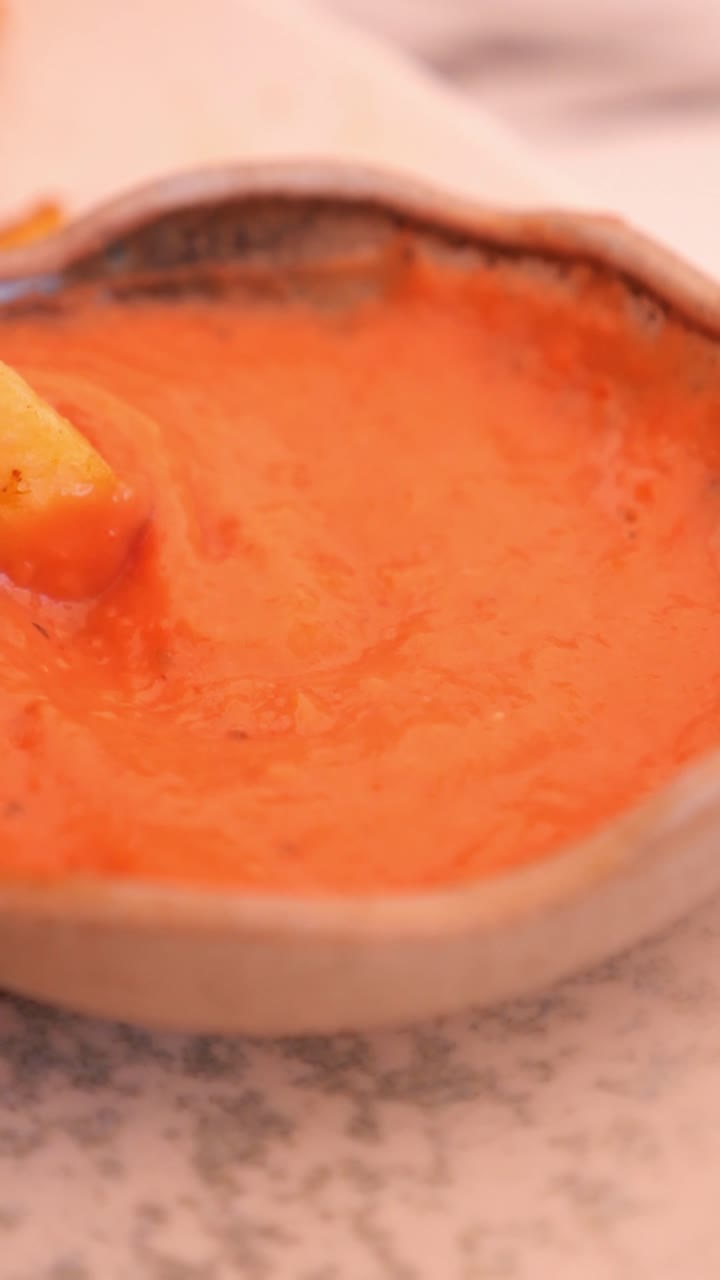 Primo piano di una mano che intinge una patatina fritta in salsa rossa.