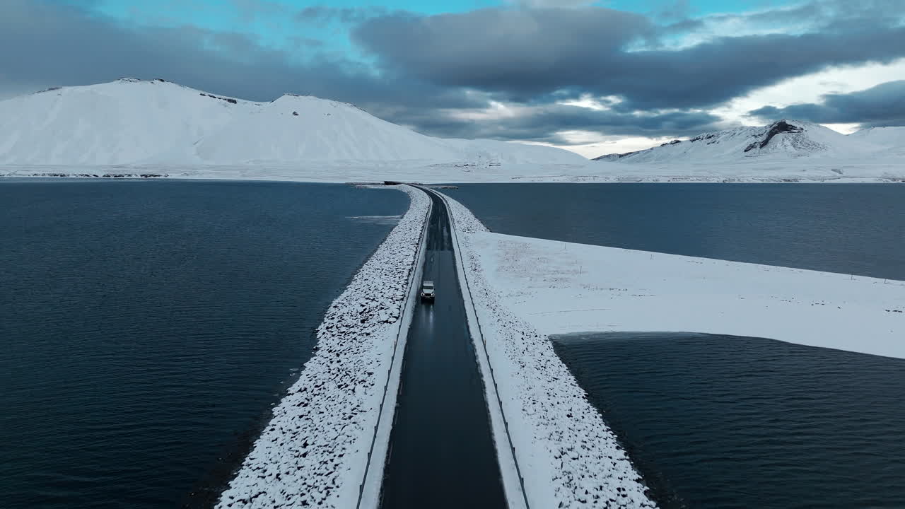 Kolgrafarfjörður Winter, Aerial Front Tracking Shot of White Jeep Traveling Down Busy Iceland Highway Bridge