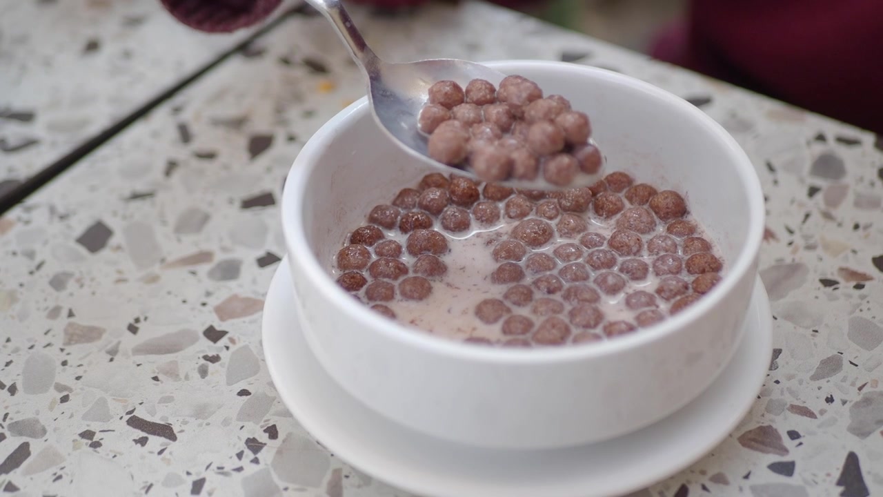 Primo piano di una mano che mescola cereali al cioccolato con latte in una ciotola bianca