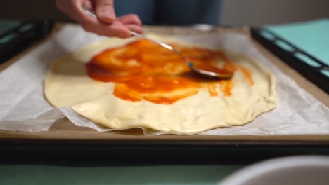 mujer esparciendo tomate en masa de pizza haciendo círculos con una cuchara