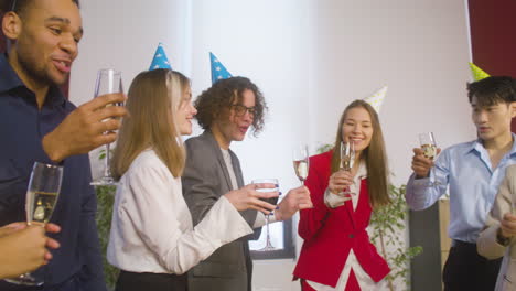 multiethnic colleagues with party hat toasting and drinking at the office party 3