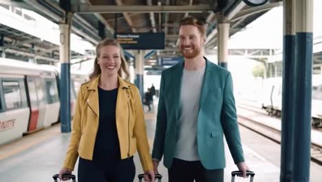 happy young couple with rolling luggage walking together at a train station platform