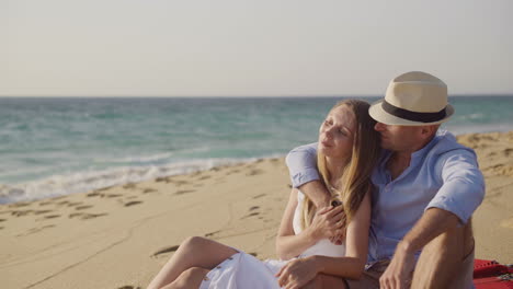 Couple-sitting-on-plaid-and-hugging-at-seaside