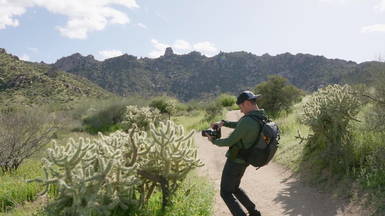 hombre caucásico se detiene a tomar fotos de un cactus en una caminata en el paisaje de montaña del desierto de arizona en el verano