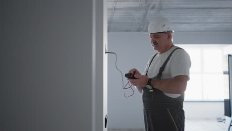 un electricista masculino comprueba el voltaje en la red con un probador de cables que se prepara para instalar una casa inteligente en un sitio de construcción.