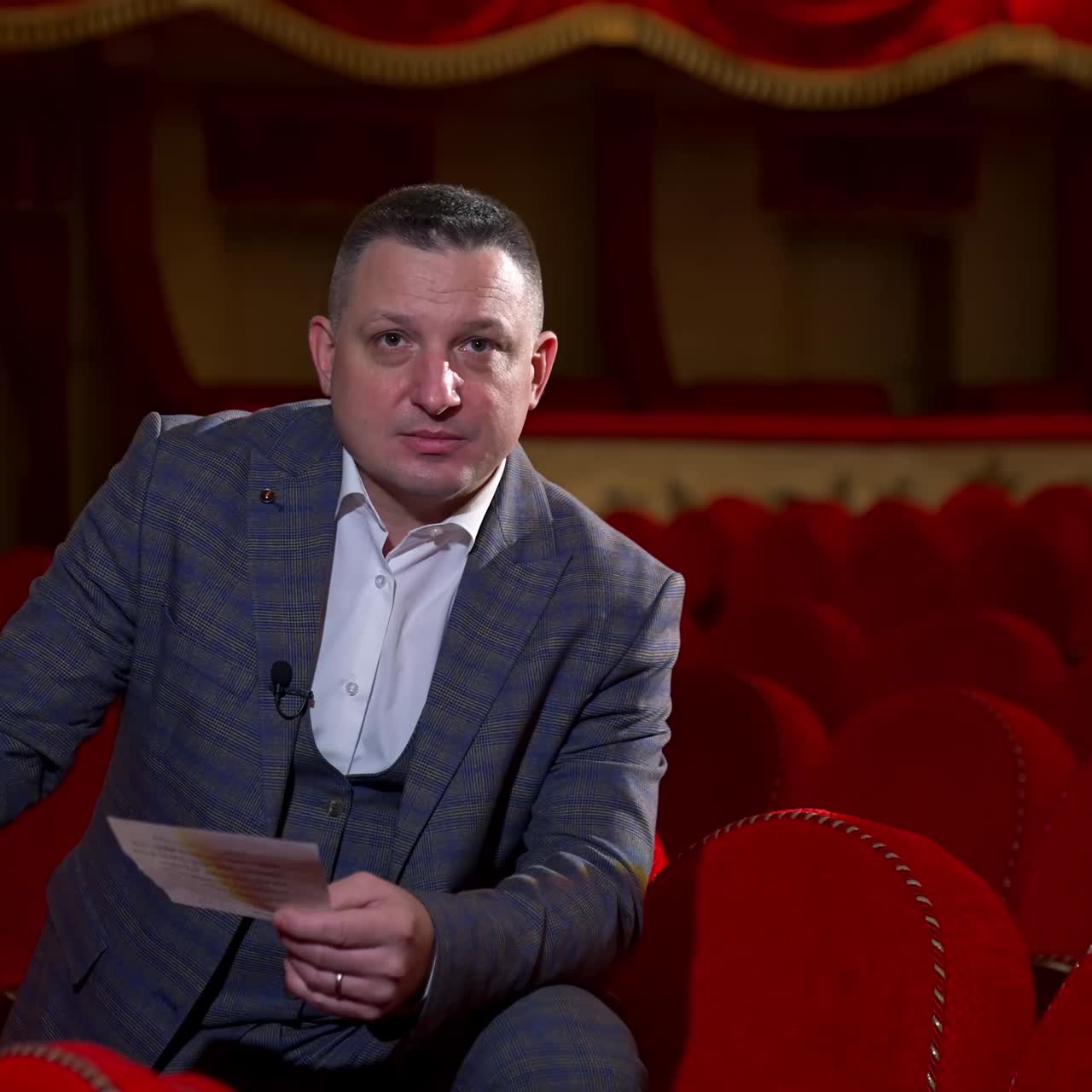 Man in costume reads a script. Medium shot of an actor rehearsing in empty theater among red chairs. Acting lifestyle