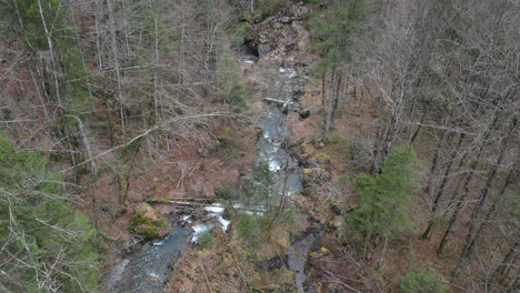 Vogelperspektive-über-Dem-Fluss,-Der-Zwischen-Großen-Felsbrocken-Und-Umgestürzten-Bäumen-Hindurch-In-Eine-Offene-Wiese-Mit-Unterholzabfällen-Fließt