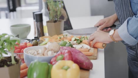 sección media de una mujer biracial preparando comida, cortando verduras en la cocina, cámara lenta