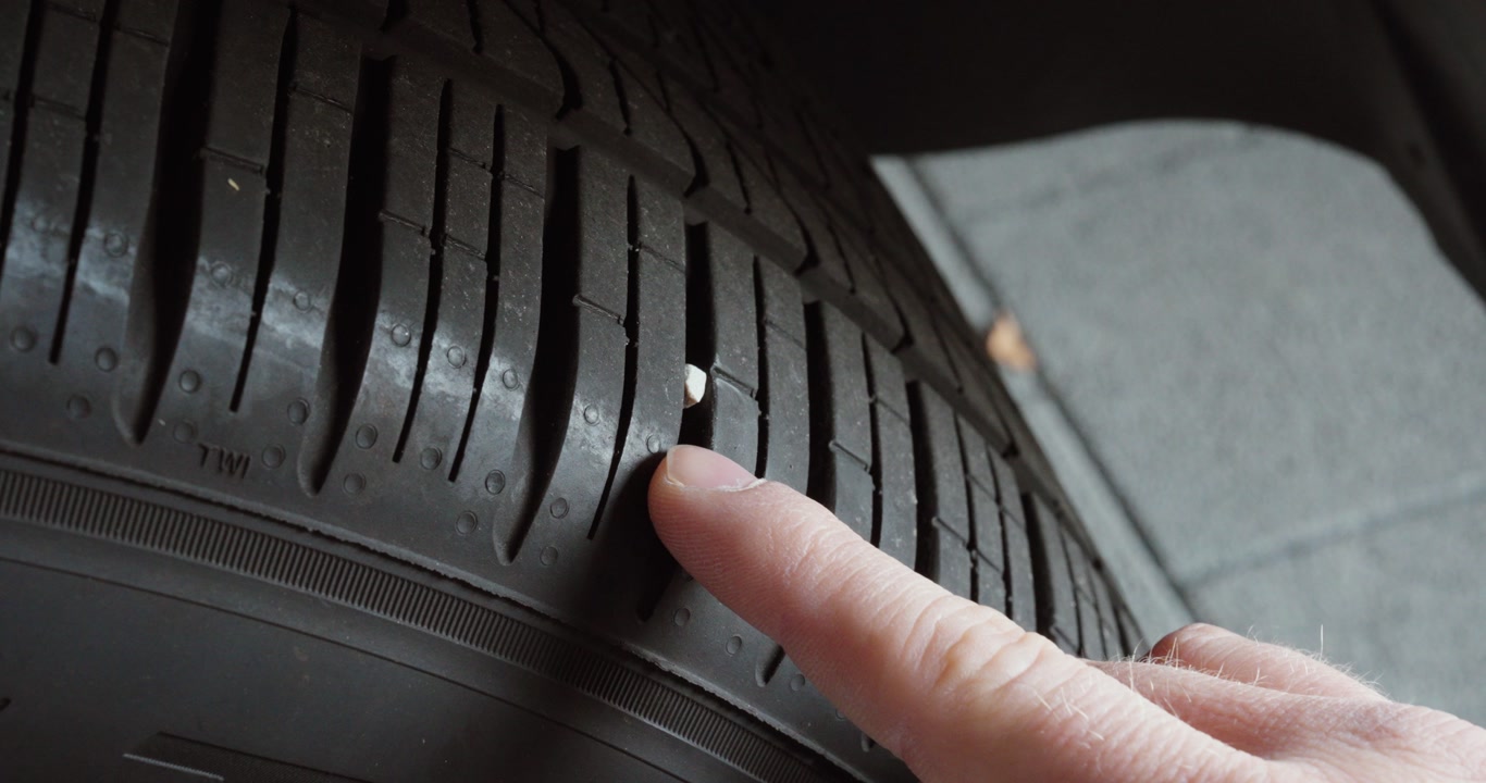 Close-up of a finger pointing at a stone stuck in a car tire tread. Concept of tire damage, safety risk and vehicle inspection.